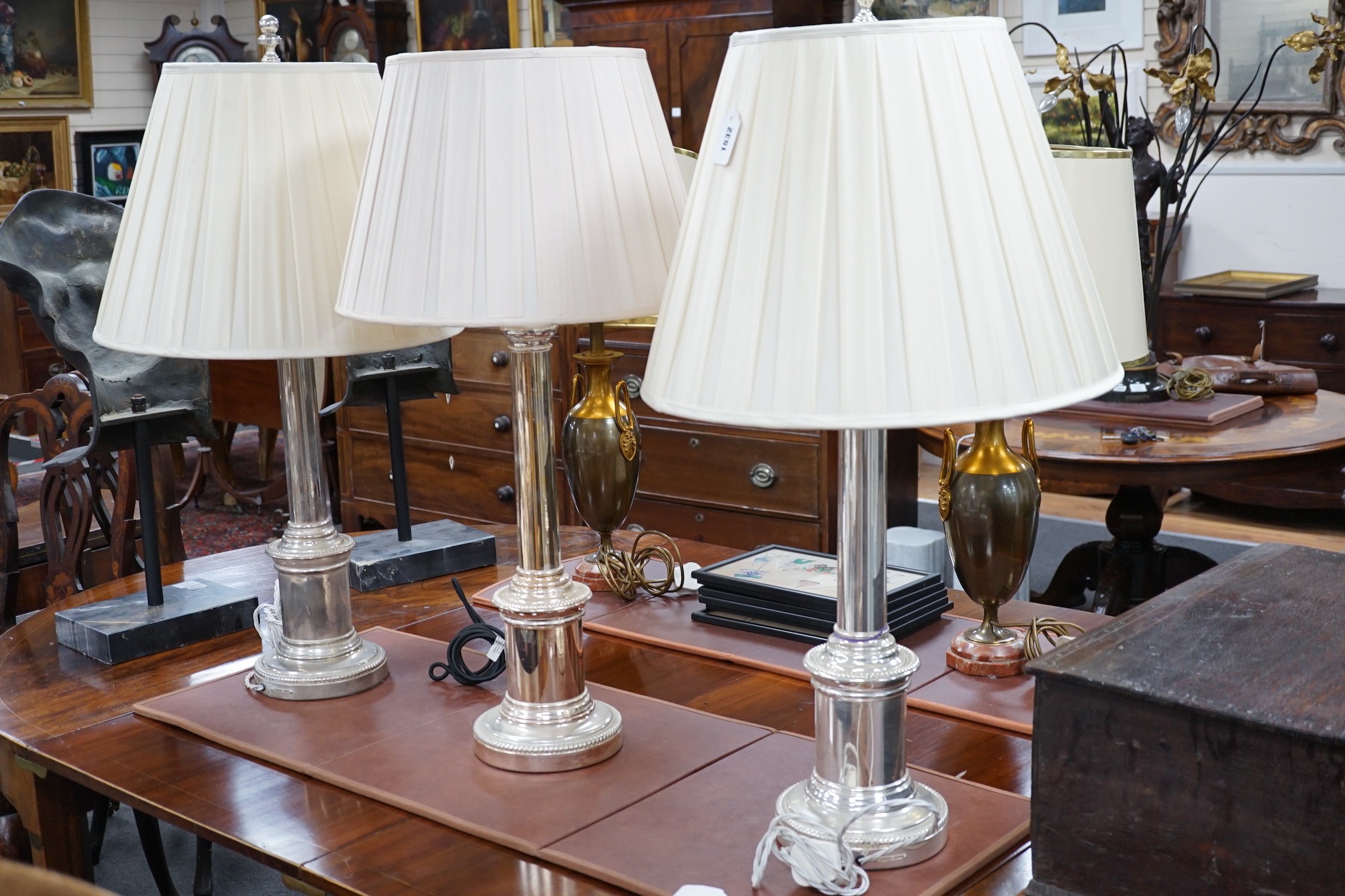 A pair of steel column table lamps, with matching cream silk shades and another similar lamp and shade, pair 96cms high